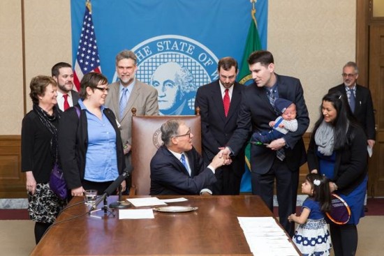 Rep. Steve Bergquist, holding newborn son, Anton, as his wife, Dr. Avanti Bergquist, and daughter, Anjali, look on, is congratulated by Gov. Jay Inslee.