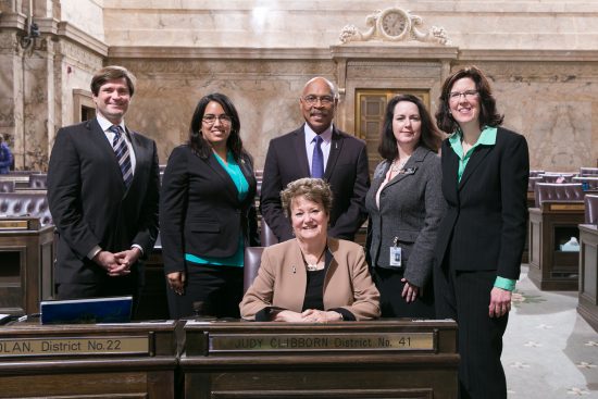 Rep. John Lovick (D-Mill Creek, center) on the floor of the House of Representatives with Rep. Mike Pellicciotti, Rep. Krstine Reeves, Transportation Chair Rep. Judy Clibborn (seated), Rep. Shelley Kloba and Rep. Christine Kilduff.