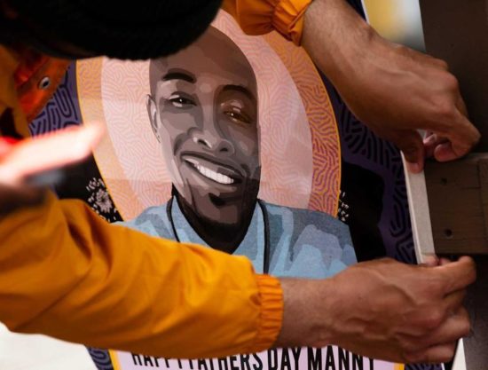 A pair of hands tapes down an illustrated poster depicting Manny Ellis smiling in a blue shirt.