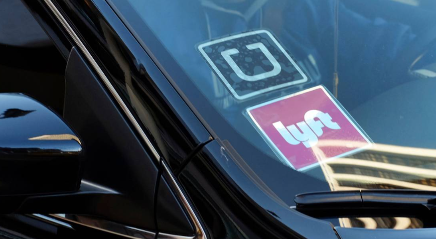 A ride share car displays Lyft and Uber stickers on its front windshield.