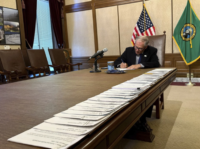Washington Gov. Jay Inslee signs bills at the Washington State Capitol, Tuesday, May 9, 2023, in Olympia, Wash. One of those bills was Senate Bill 5599, which was designed to protect young people seeking reproductive health services or gender-affirming care.