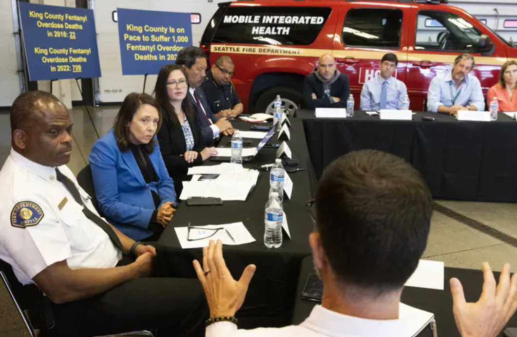 U.S. Senator Maria Cantwell (2nd from left) listens to Brad Finegood (back to camera at right) of Public Health – Seattle & King County as she holds a roundtable with local leaders about the fentanyl crisis in Washington. In the background is a new mobile fire department unit that responds to overdoses.