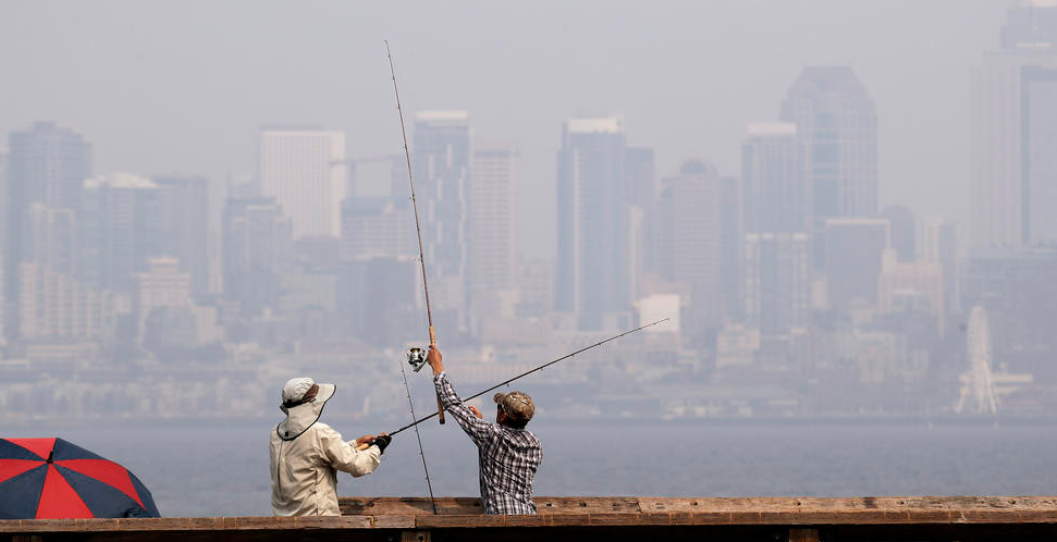 A pair of anglers uncross their lines while fishing in Elliott Bay as a smoky haze obscures downtown Seattle on Tuesday, Aug. 14, 2018.