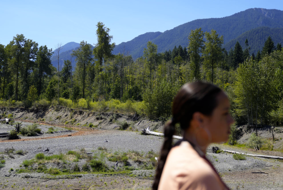 Lacy Bowles listens to a presentation at the former Aldwell Lake along the Elwha River, which drained and was revegetated after the removal of the Elwha Dam, during the 2023 Tribal Climate Camp on the Olympic Peninsula Wednesday, Aug. 16, 2023, near Port Angeles. Participants representing at least 28 nations and intertribal organizations gathered to connect and share knowledge as they work to adapt to climate change that disproportionally affects Indigenous communities. More than 70 nations have taken part in the camps, which have been held across the United States since 2016.