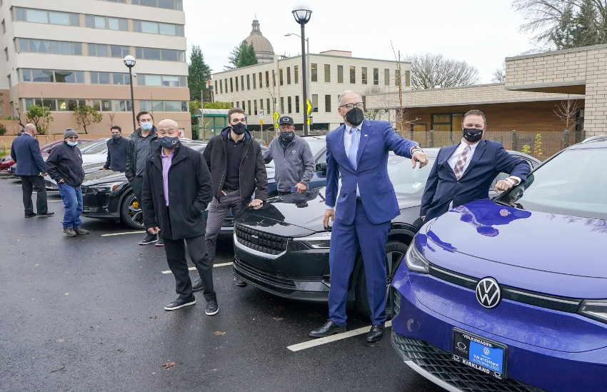 Washington Gov. Jay Inslee, second from right, walks through a car dealership for an electric vehicle news conference in 2021. The number of electric cars just surged in Washington, showing Inslee’s dream of an EV age may come true. But whole regions of the state are not joining.