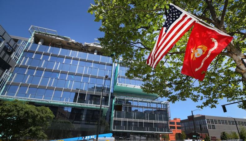 A U.S. flag and Marine Corps flag flew next to a photo mounted on a tree near where four people were killed on April 27, 2019, when a tower crane collapsed on part of Google's new South Lake Union campus in Seattle. Two state legislators on Wednesday announced plans to introduce legislation to regulate how construction cranes are set up and disassembled.