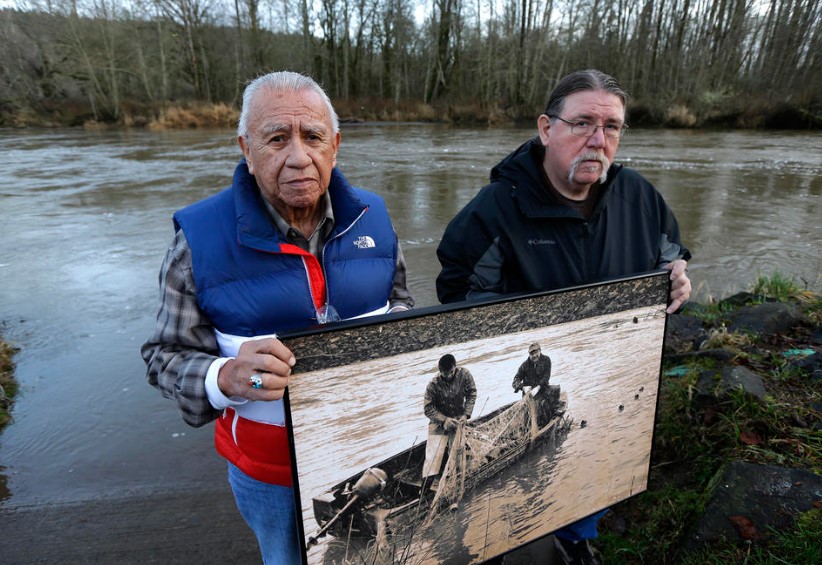 Billy Frank Jr., left, a Nisqually tribal elder who was arrested dozens of times while trying to assert his Native fishing rights during the Fish Wars of the 1960s and ’70s, poses for a photo Monday, Jan. 13, 2014, with Ed Johnstone, of the Quinault tribe, at Frank’s Landing on the Nisqually River in Nisqually, Wash. They are holding a photo from the late 1960s of Frank and Don McCloud fishing on the river.
