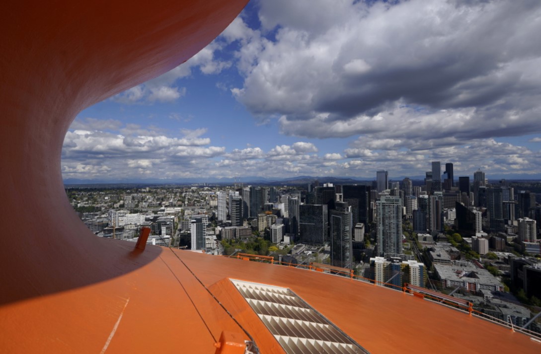 Downtown Seattle is framed by the curved roof of the Space Needle, Tuesday, May 10, 2022, in Seattle. The roof of the Seattle icon has been painted its original color of 
