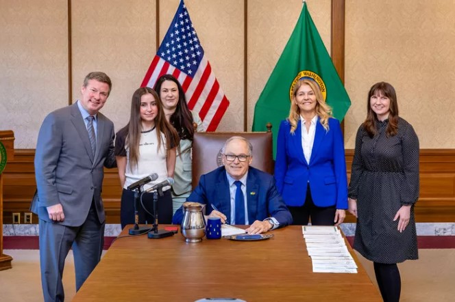 Gov. Jay Inslee signs a bill relating to fabricated intimate or sexually explicit images and depictions with primary sponsor Rep. Tina Orwall, right, and Caroline Mullet who testified in support, left, on Thursday in Olympia. 