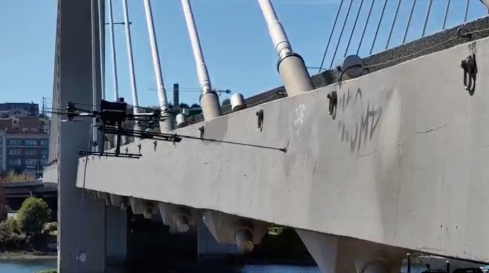 A drone equipped with spray paint covers over graffiti at a hard-to-reach spot along Tacoma's East 21st Street Bridge. WSDOT is experimenting with drones in limited areas in Tacoma and Olympia that can paint over graffiti.