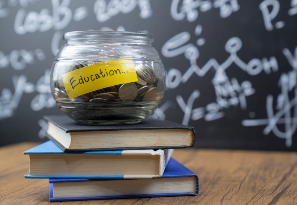 Photo of a stack of three books with a bowl of quarters on top. There is a yellow piece of paper inside the bowl that says “education”.