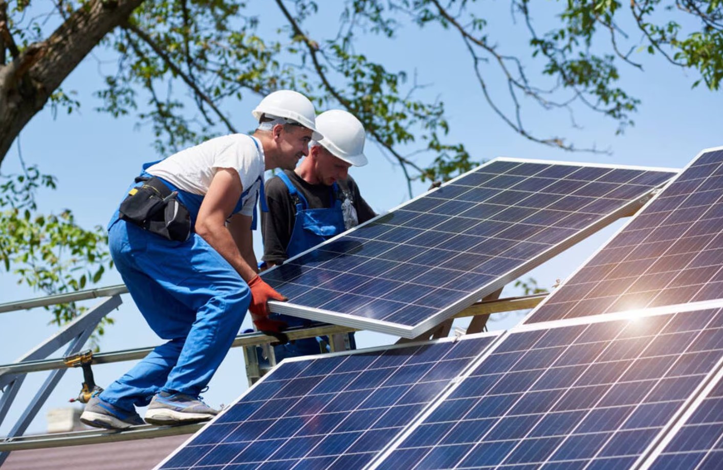 Two workers installing solar panels on a roof