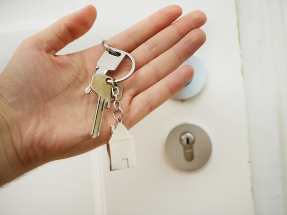 Photo of a person’s hand holding keys to a house with a door in the background.