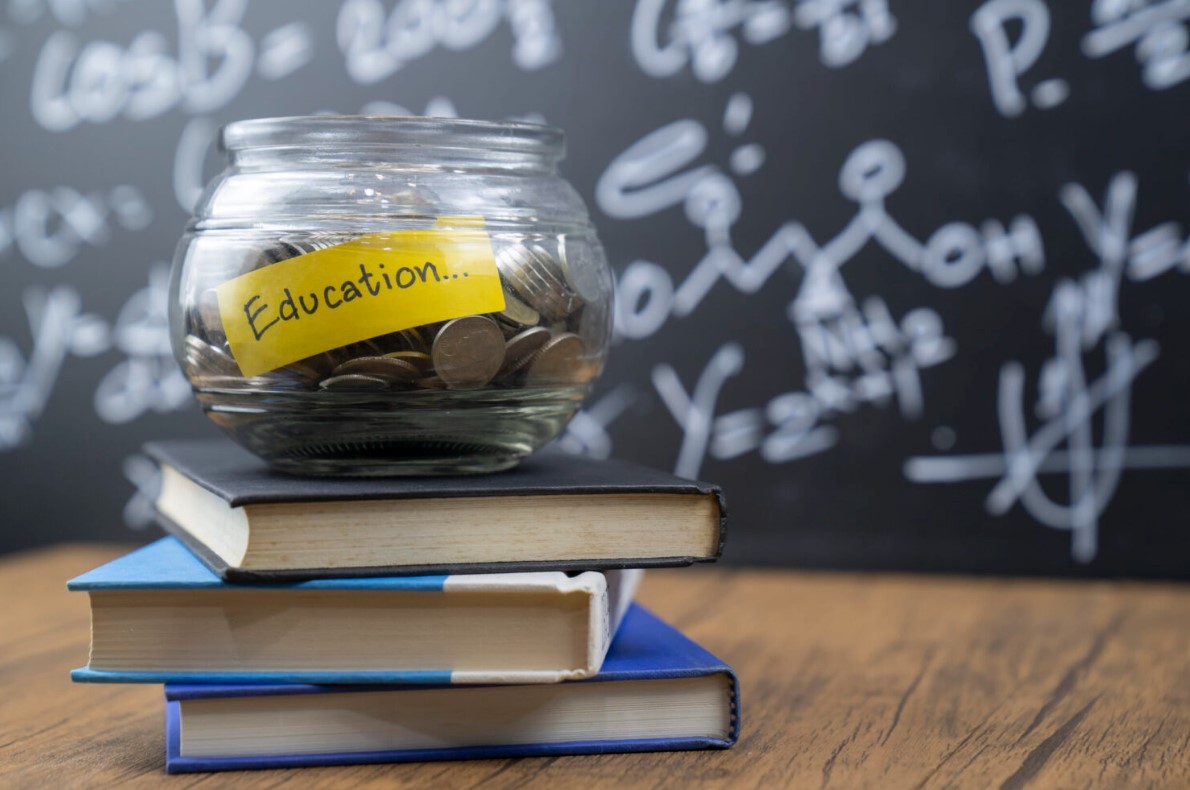 Stack of books on a desk with a bowl labeled “education” on top.