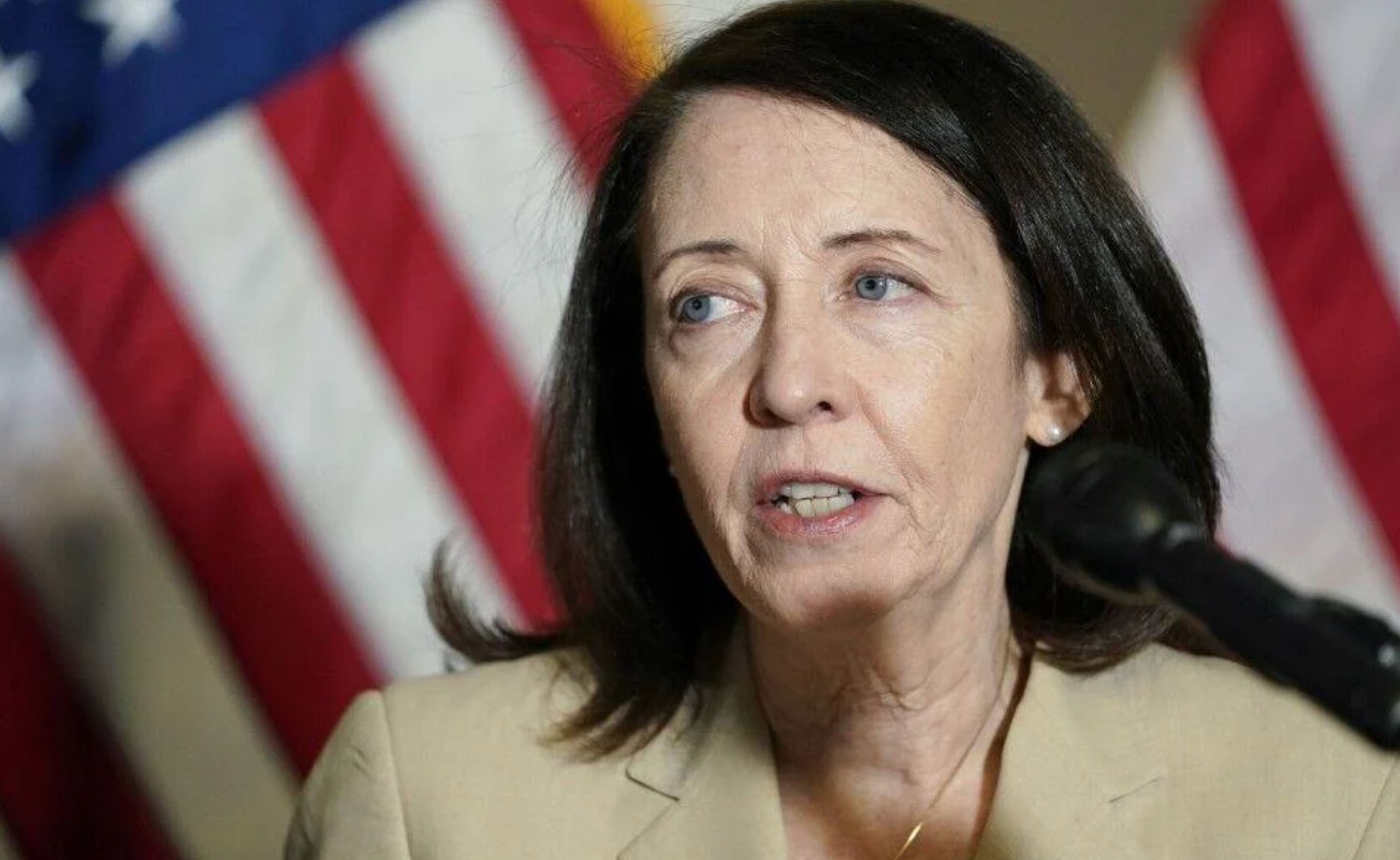 Photo of Senator Maria Cantwell speaking into a microphone with an American flag behind her.