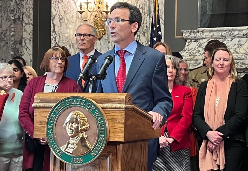 Washington state Attorney General Bob Ferguson (at podium) makes remarks prior to Gov. Jay Inslee (to the left of Ferguson) signing a package of gun legislation in April 2023. (Bill Lucia/Washington State Standard)