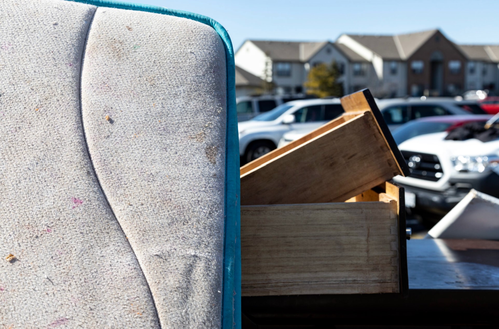 Close up photo of a mattress and dresser drawers in the parking lot of a multi-family housing complex.