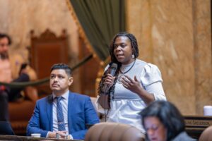 Rep. Jamila Taylor speaking on the floor of the house with Rep. Julio Cortes listening in the background