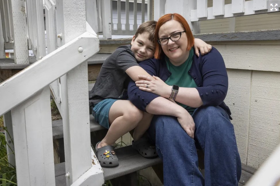 Erin Nunn sits on the front porch of the family’s Tukwila home with one of her sons, 11-year-old Geoffrey. Nunn says registering her kids in summer camps feels like a side job. (Ellen M. Banner / The Seattle Times)