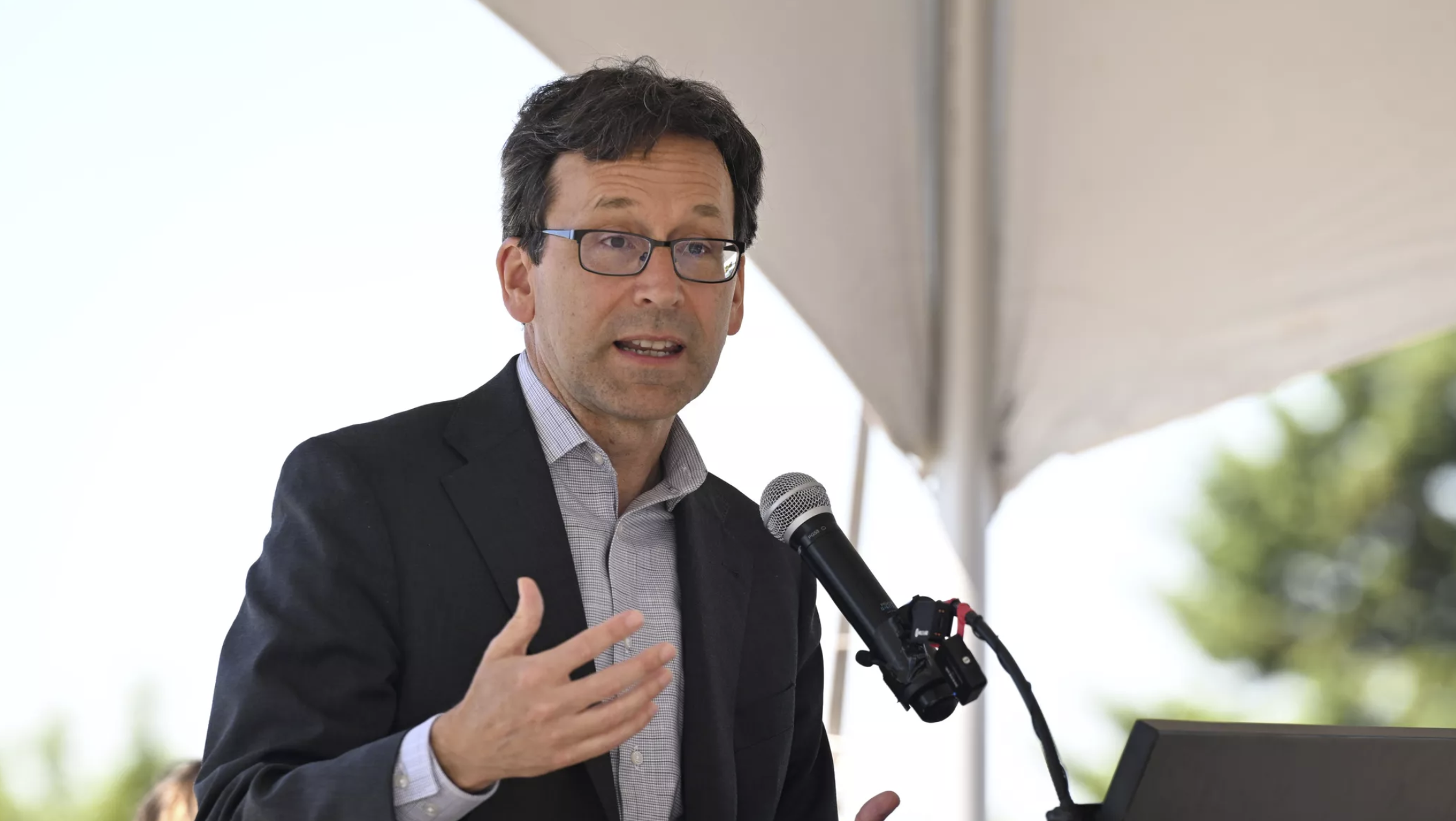 Under a tent, Washington Governor Bob Ferguson addresses the media and groups of workers involved in completing the North Spokane Cooridor at an event last month. Ferguson has condemned the One Big Beautiful Bill Act signed this month by President Donald Trump. (Jesse Tinsley/The Spokesman-Review)