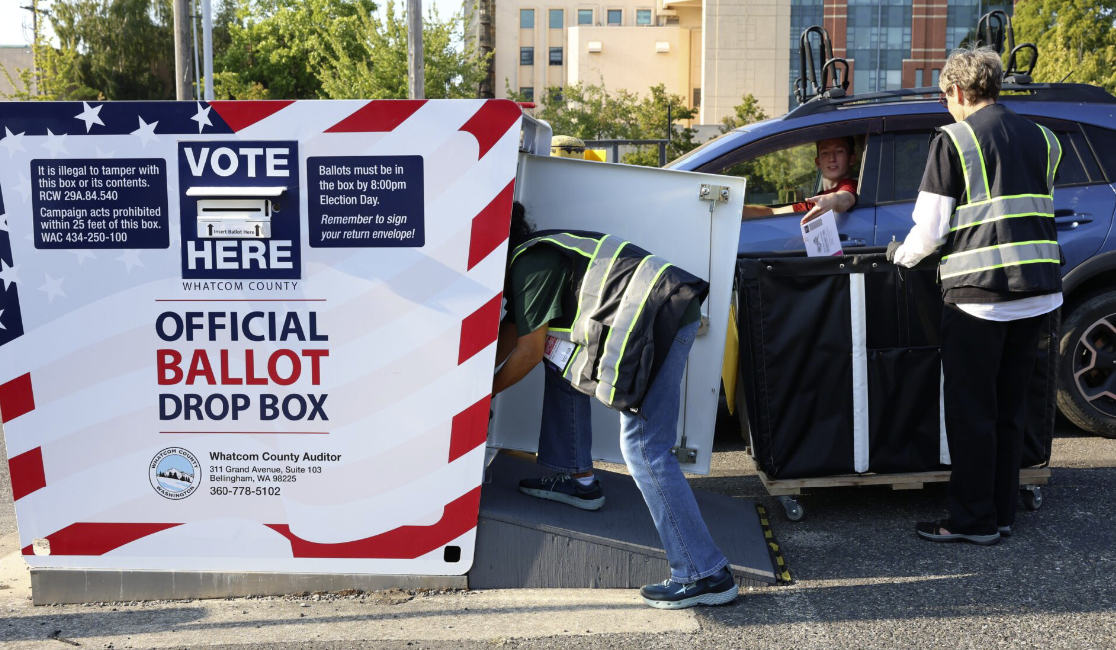 Elections coordinator Arcenia Huerta, left, and elections worker Cam Kerst remove ballots from the ballot box outside the Whatcom County Courthouse in August 2024. Elections employees work in pairs when transferring ballots to ensure security. (Hailey Hoffman/Cascadia Daily News)