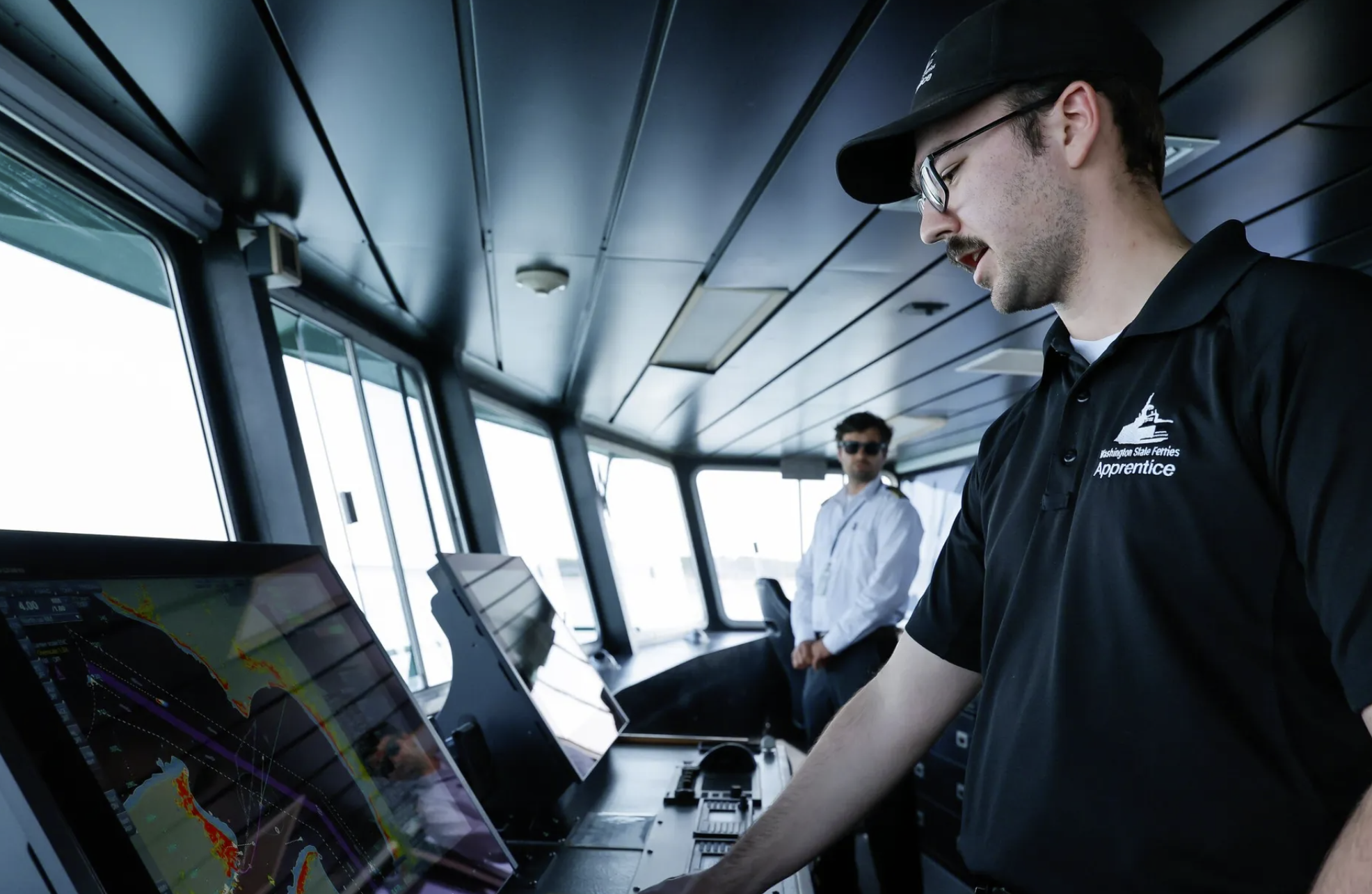 Apprentice Adam Knutsen looks at his screens as he navigates the ferry Kennewick, under the watchful eye of Capt. Jesse Rongo, near Port Townsend in June. Apprenticeship programs are growing across the state. (Jennifer Buchanan / The Seattle Times)