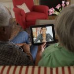 African American elderly couple on couch video chatting with granddaughter.