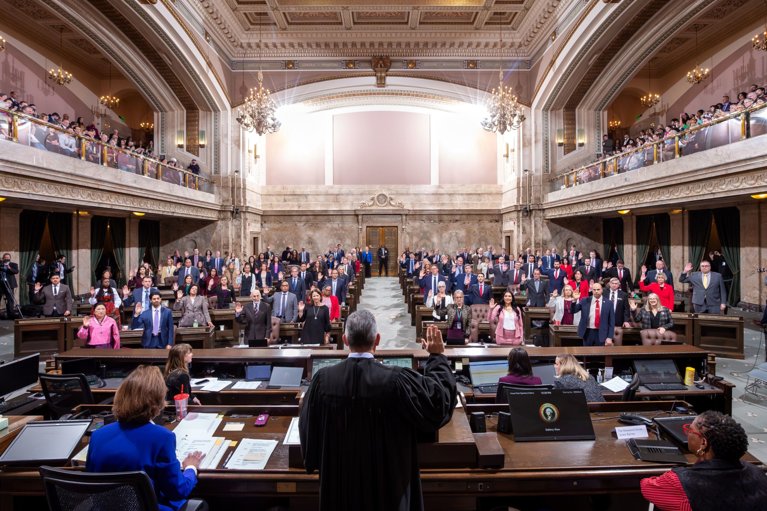 Image taken from behind a judge as he looks out at dozens of elected members who all have their right hands raised.