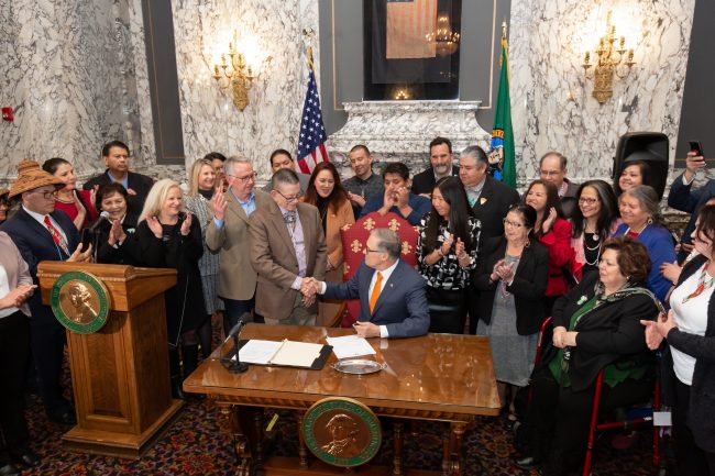 Photo of crowd at bill signing for SB 5079. Crowd is clapping, Governor is shaking Sen. McCoy's hand.