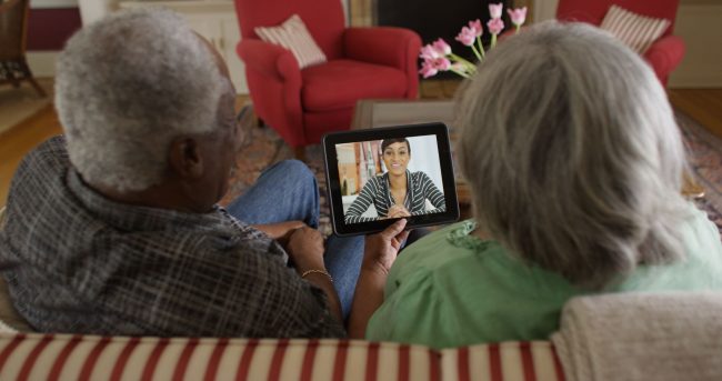 African American elderly couple on couch video chatting with granddaughter.