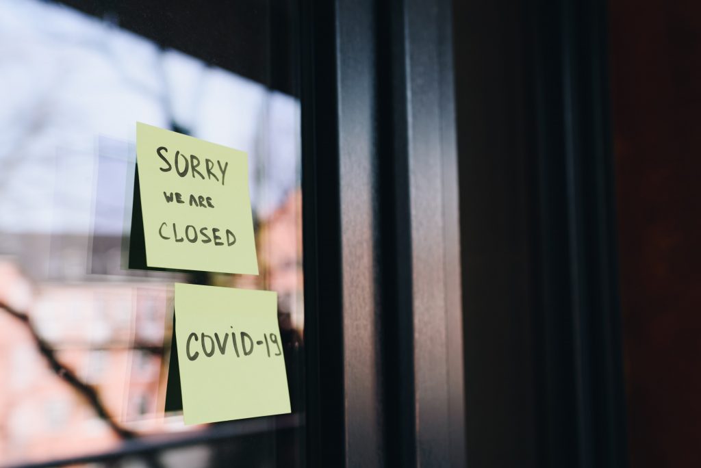 Two yellow post it notes on glass door that say Sorry We are closed and "Covid 19"