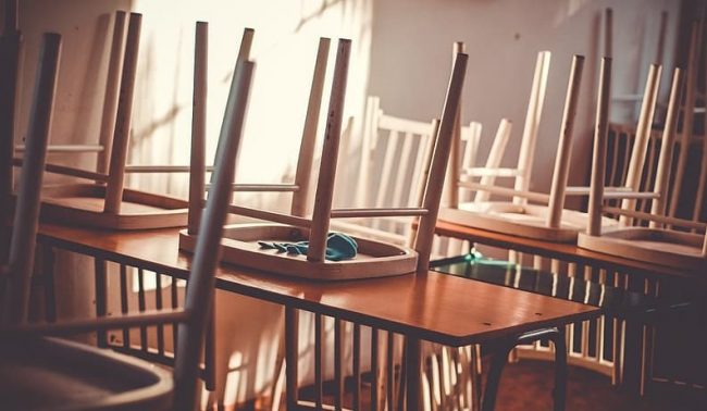 wooden chairs turned upside down on tables in closed restaurant, light streaming in through window