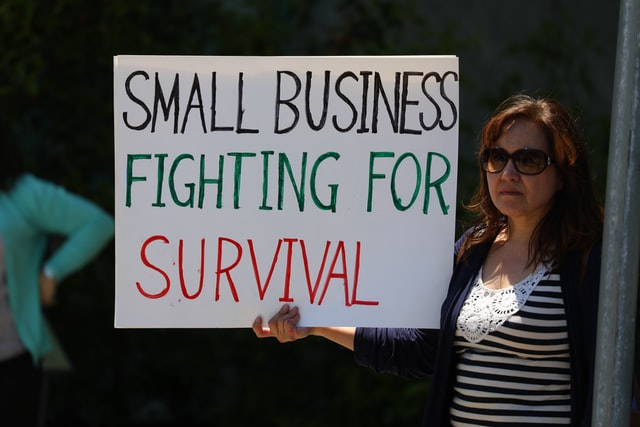 Woman holding sign that says "Small Business Fighting for Survival"