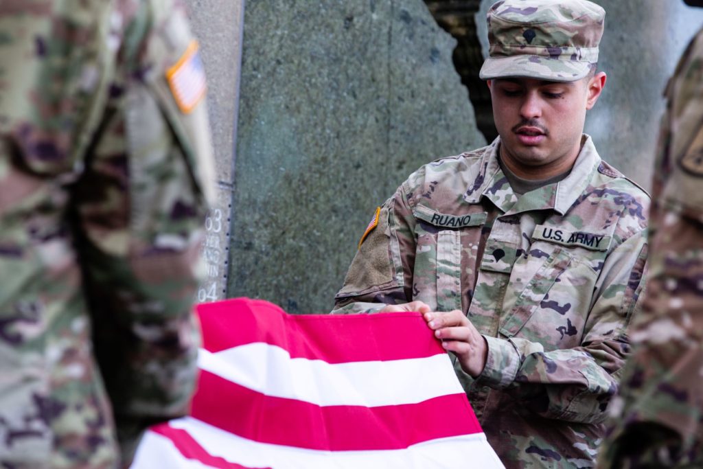 Military member in camo holding folded flag