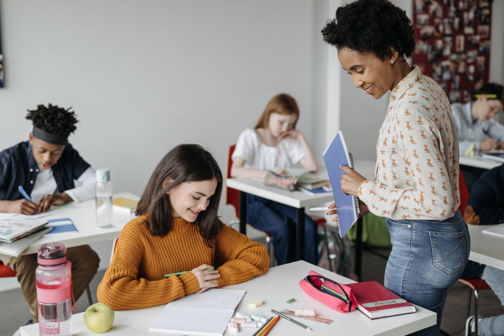 Teacher standing by student desk smiling