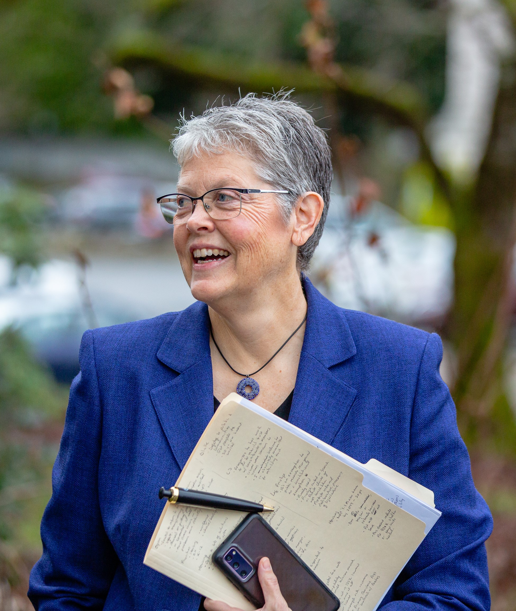 Speaker Jinkins smiling, holding her phone and a folder of paper, while walking outside