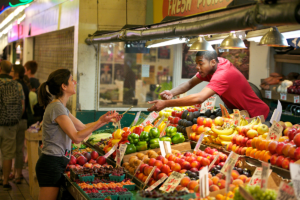 Photo of a man handing an item to a woman at a fruit stand.