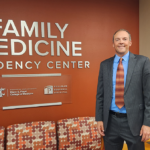 Rep. Marcus Riccelli standing in front of a wall with a sign that says FAMILY MEDICINE RESIDENCY CENTER WASHINGTON STATE UNIVERSITY ELSON S. FLOYD COLLEGE OF MEDICINE and PULLMAN REGIONAL HOSPITAL