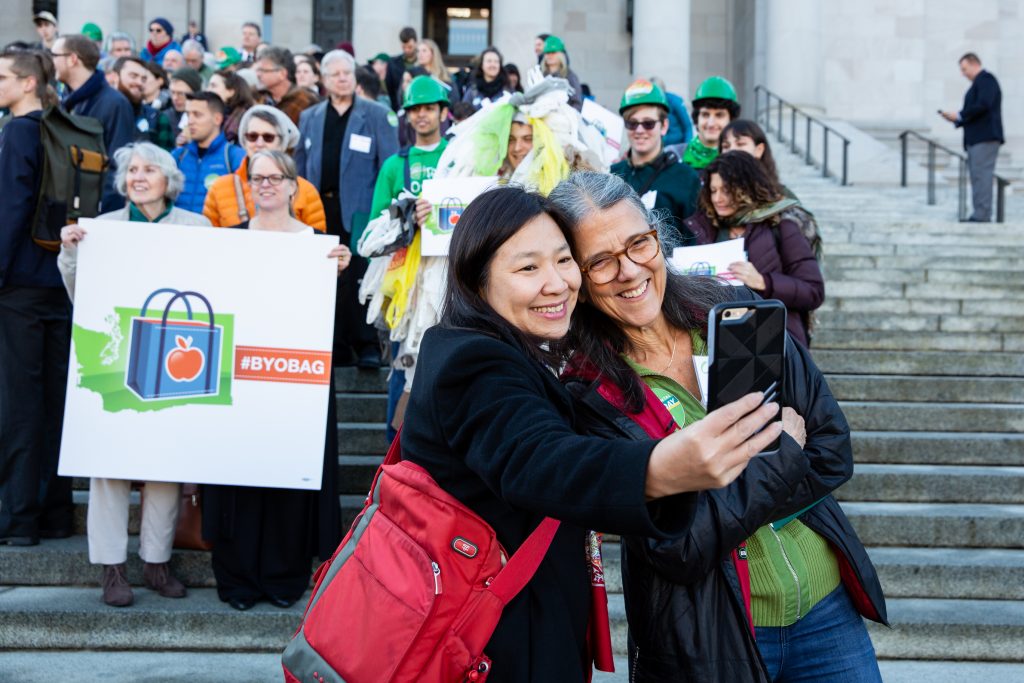 Rep. Thai and woman with glasses take selfie in front of capitol building at Environmental Priorities Coalition Rally