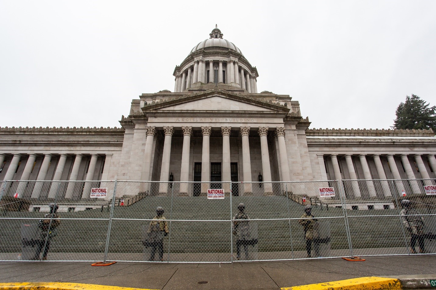 National Guard solider stand behind a fence in front of the steps of the Washington State Capitol