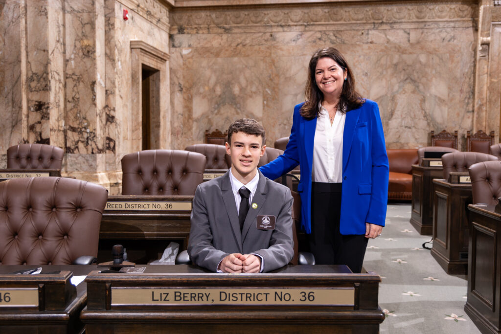 Page Damian Miller sitting at Rep. Berry's desk on the House of Representatives with Rep Liz Berry standing beside him on January 30 2025